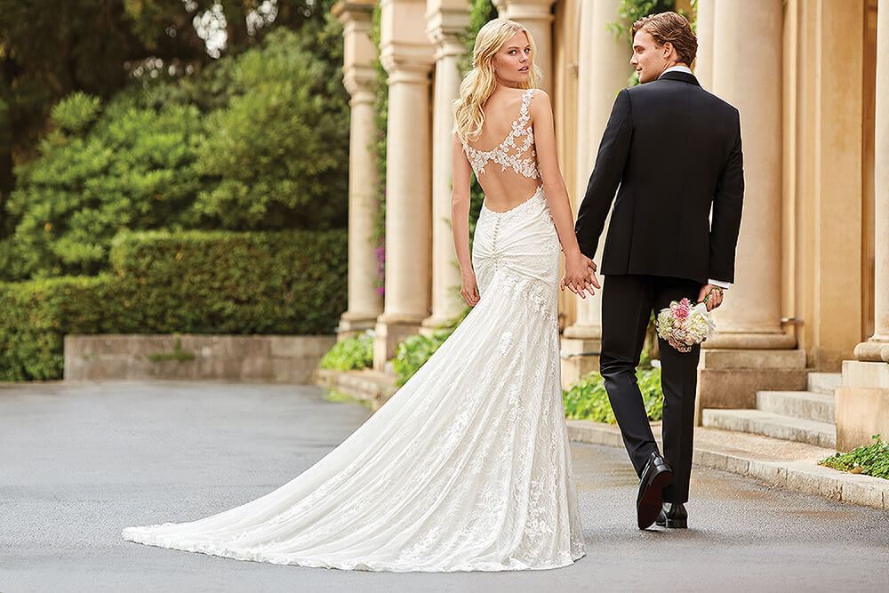 A model wearing a fit and flare lace wedding dress in a styled shoot accompanied with a male model wearing a black tuxedo