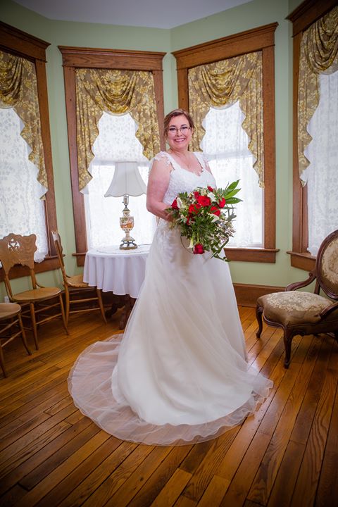 Bride in cap sleeve wedding gown posing with bouquet in a Victorian style room.