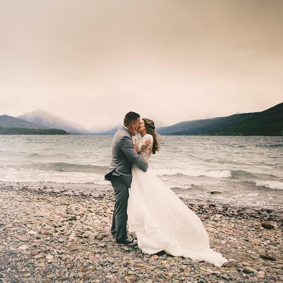 Bride and groom kissing on rocky beach.