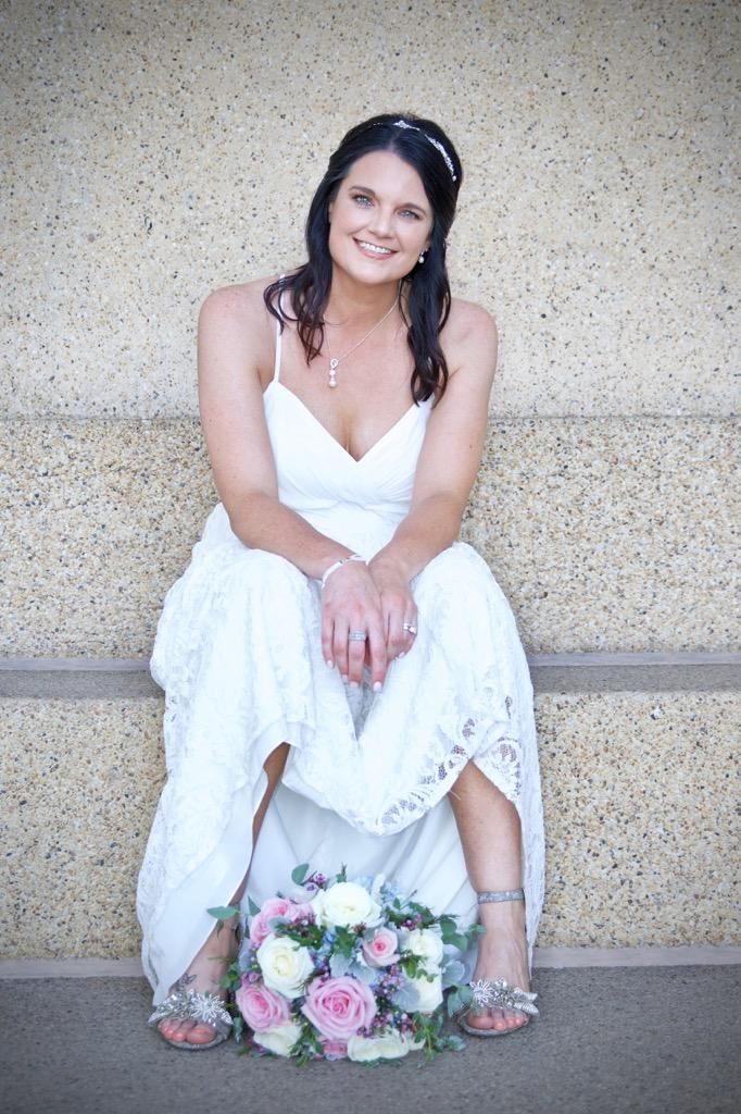 Bride in simple wedding dress sitting on a step.